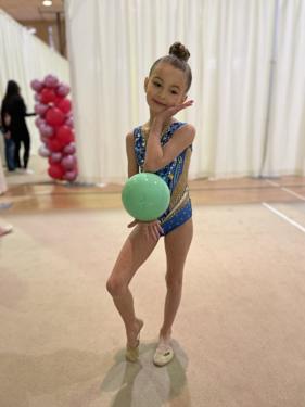 Young gymnast in a blue leotard holding her ball, ready to start a routine
