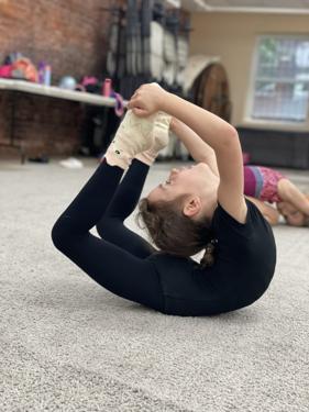 Gymnast in a deep backbend, reaching for the ball held above her head