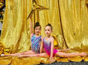 Two gymnasts holding the splits in front of a gold backdrop