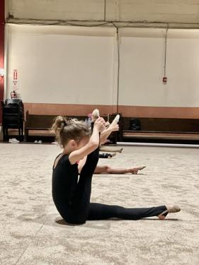 Gymnast holding a seated balance with her arms overhead in training