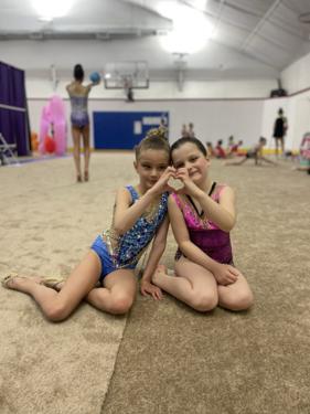 Two young gymnasts making heart signs after class
