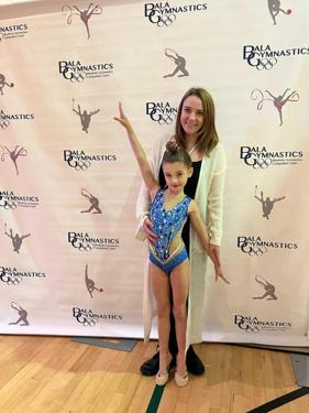 Gymnast striking her finishing pose beside her coach at the competition backdrop