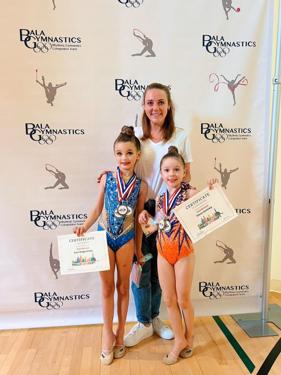 Two gymnasts with their coach, holding medals and certificates at the competition